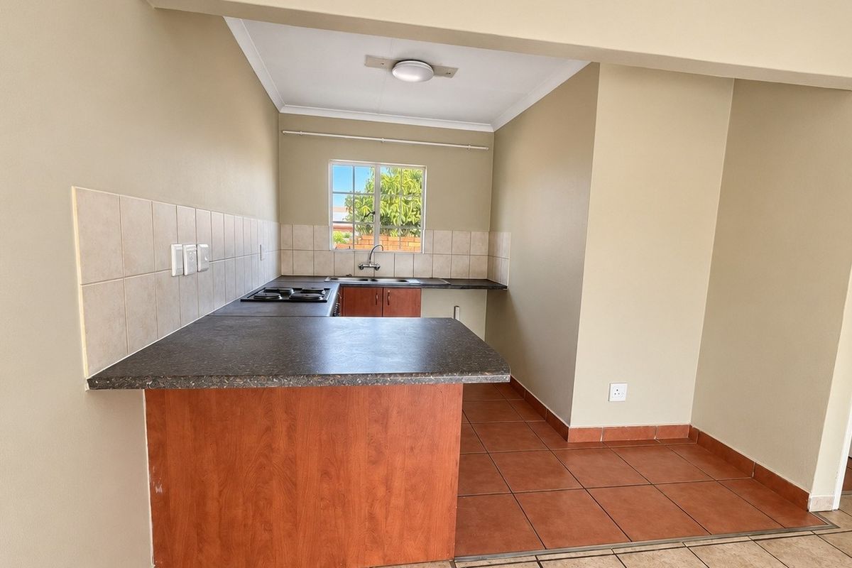 A functional kitchen featuring laminate countertops, a built-in hob, stainless steel sink, and tiled backsplash, offering a clean and practical workspace.