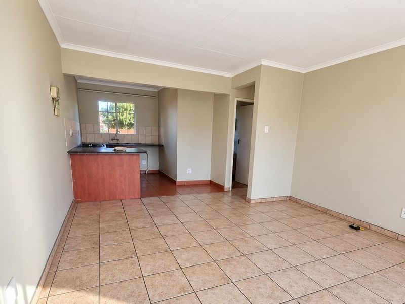 An open-plan living and kitchen area featuring tiled flooring, neutral wall tones, and functional kitchen cabinetry in a well-maintained townhouse setting.