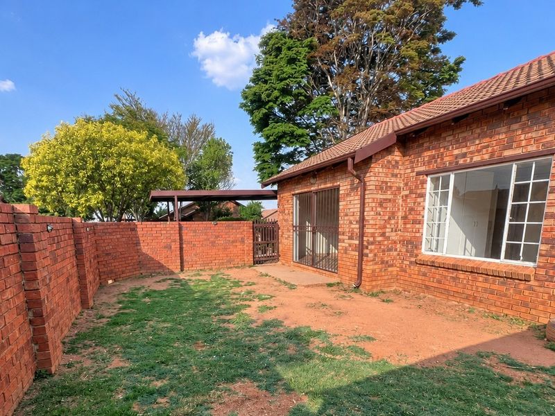 Rear view of a face brick townhouse featuring a private garden area, security gate, and tiled roof.