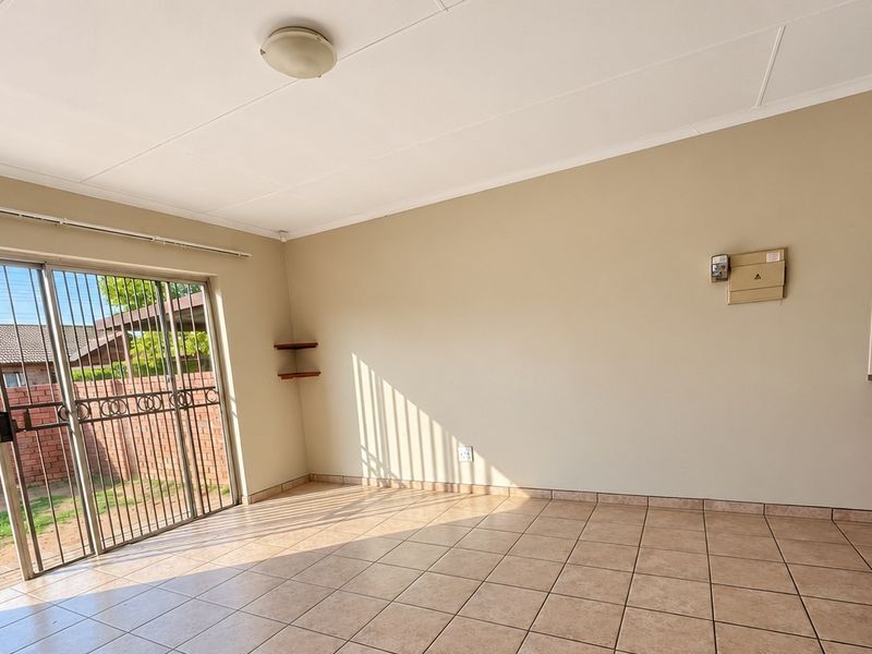An open-plan living area featuring tiled flooring, a sliding glass door with security gate, and direct access to the outdoor space.