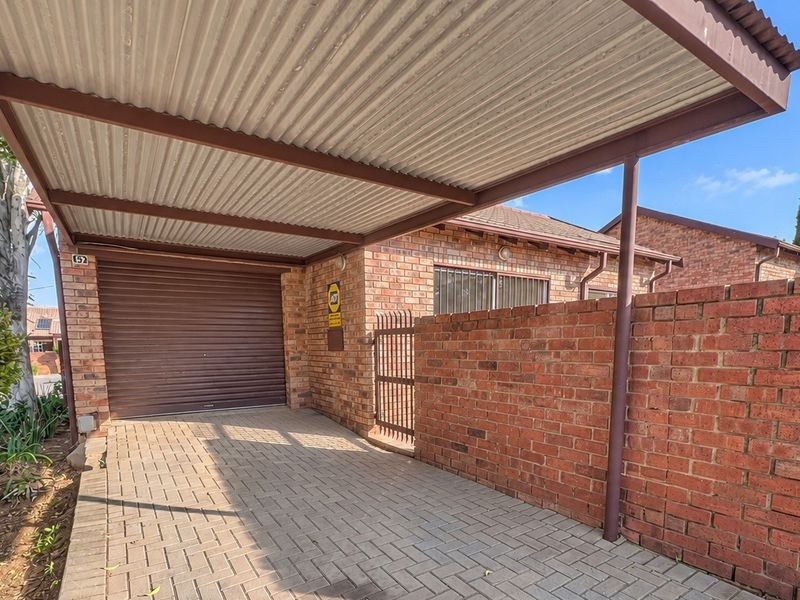 A covered carport area with a paved driveway, brick walling, and a secure roller shutter garage door entrance.
