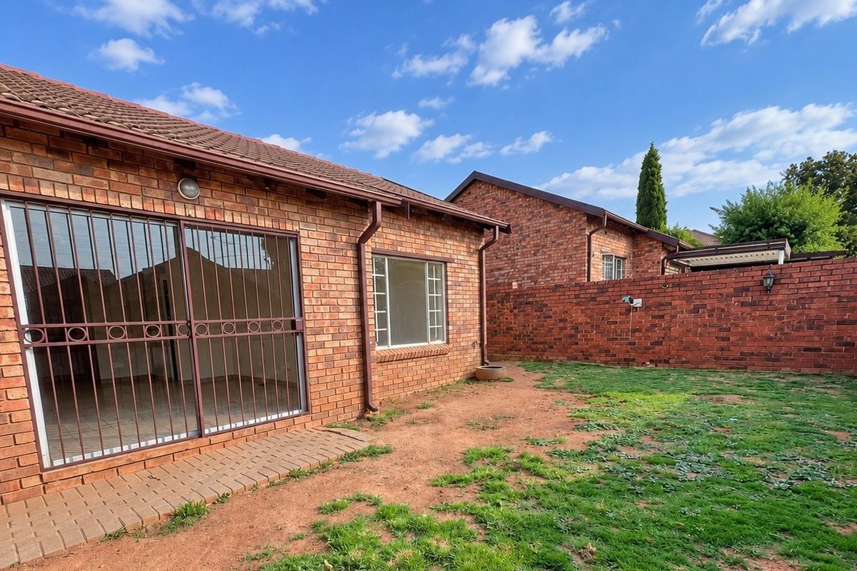 Rear view of a face brick townhouse featuring a private garden, security gate, and sliding door access to the interior.