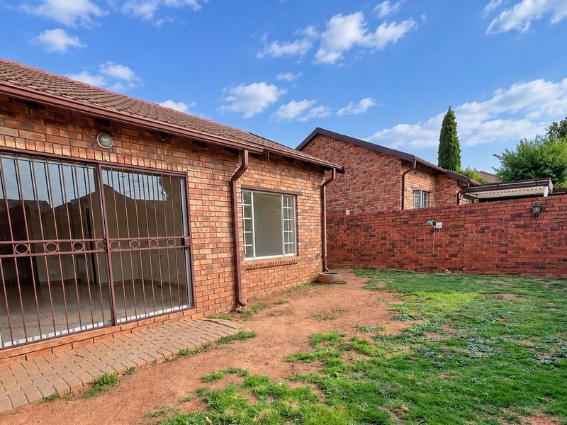 Rear view of a face brick townhouse featuring a private garden, security gate, and sliding door access to the interior.