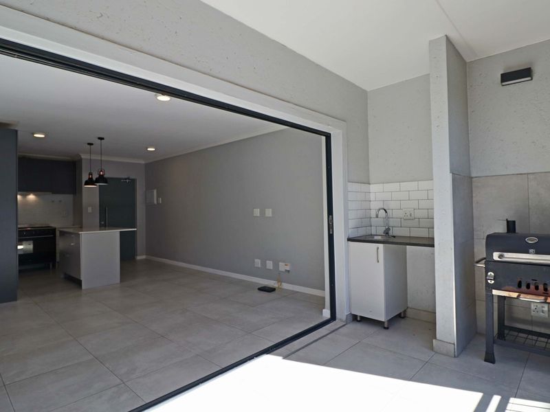 Covered patio area featuring a built-in sink, subway tile backsplash, and large sliding doors providing seamless access to the open-plan interior living space.