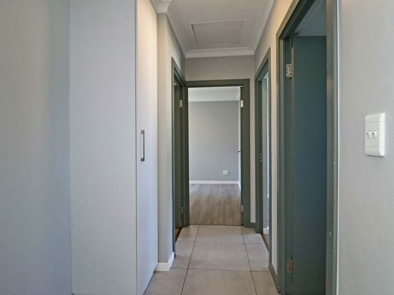 A clean and well-maintained hallway featuring neutral tiled flooring, built-in storage cabinetry, and access to adjacent rooms.