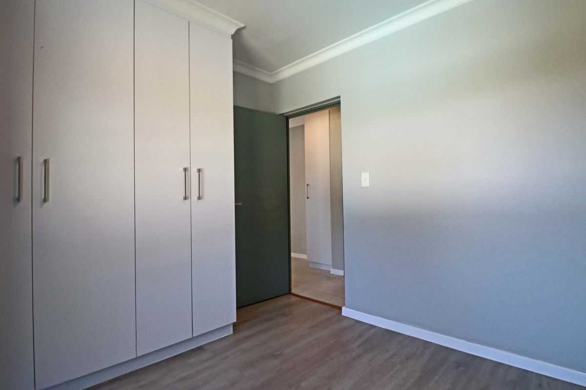 A clean, empty bedroom featuring modern laminate flooring, built-in cupboards, and neutral wall finishes, offering a versatile space ready for personalization.