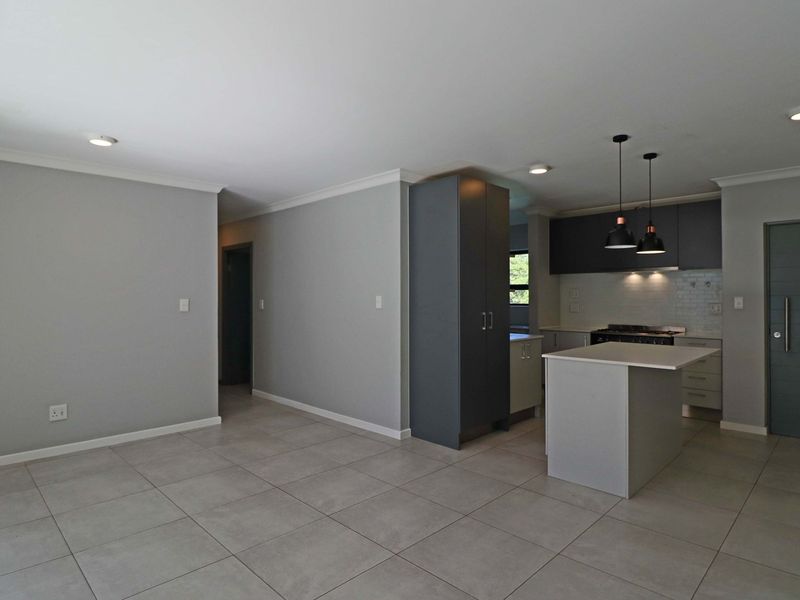 Modern open-plan living and kitchen area featuring sleek cabinetry, a central island, tiled flooring, and contemporary recessed lighting throughout.
