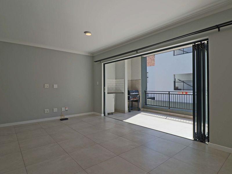 Spacious, empty living area featuring neutral tiled flooring and large bi-fold glass doors that open onto a private balcony.