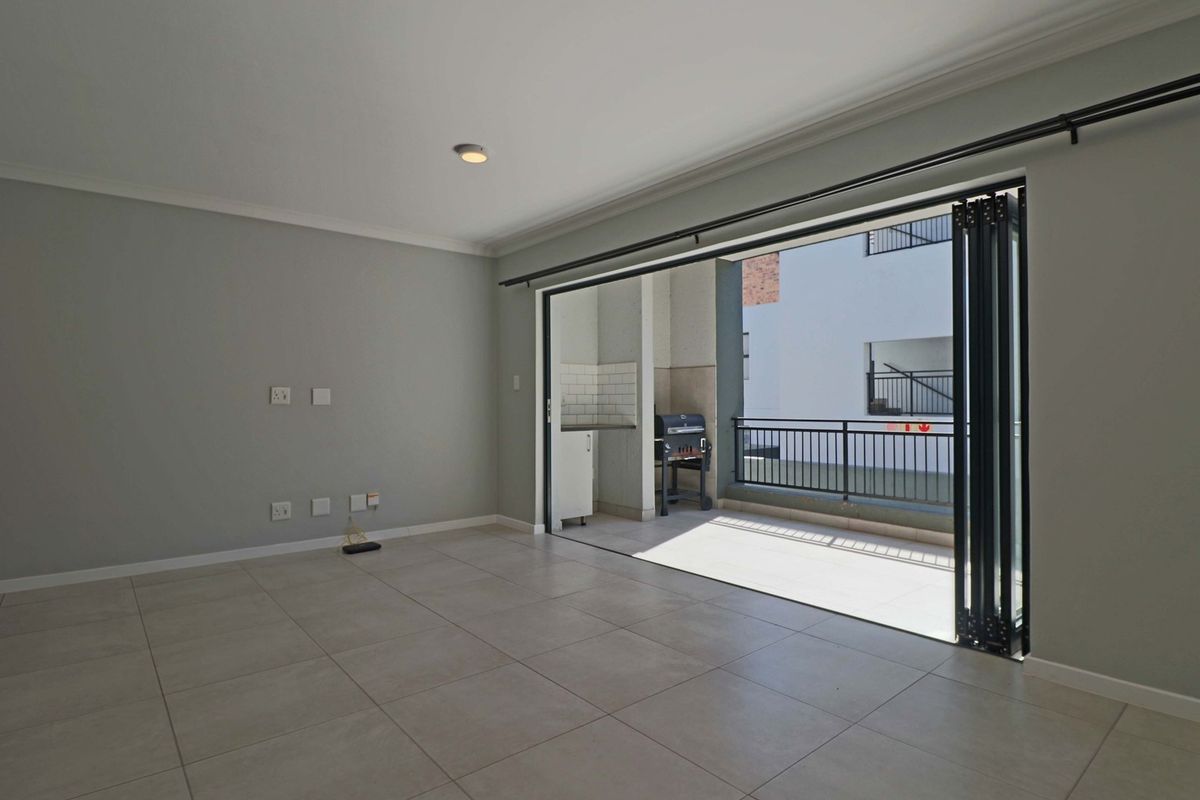 Spacious, empty living area featuring neutral tiled flooring and large bi-fold glass doors that open onto a private balcony.