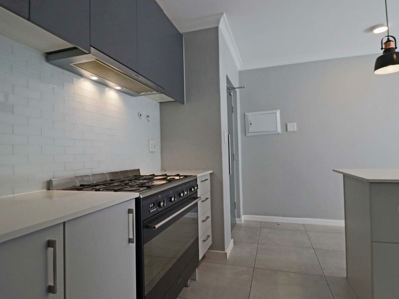 Modern kitchen featuring sleek grey cabinetry, stone countertops, a gas stove with extractor fan, and a clean subway tile backsplash.