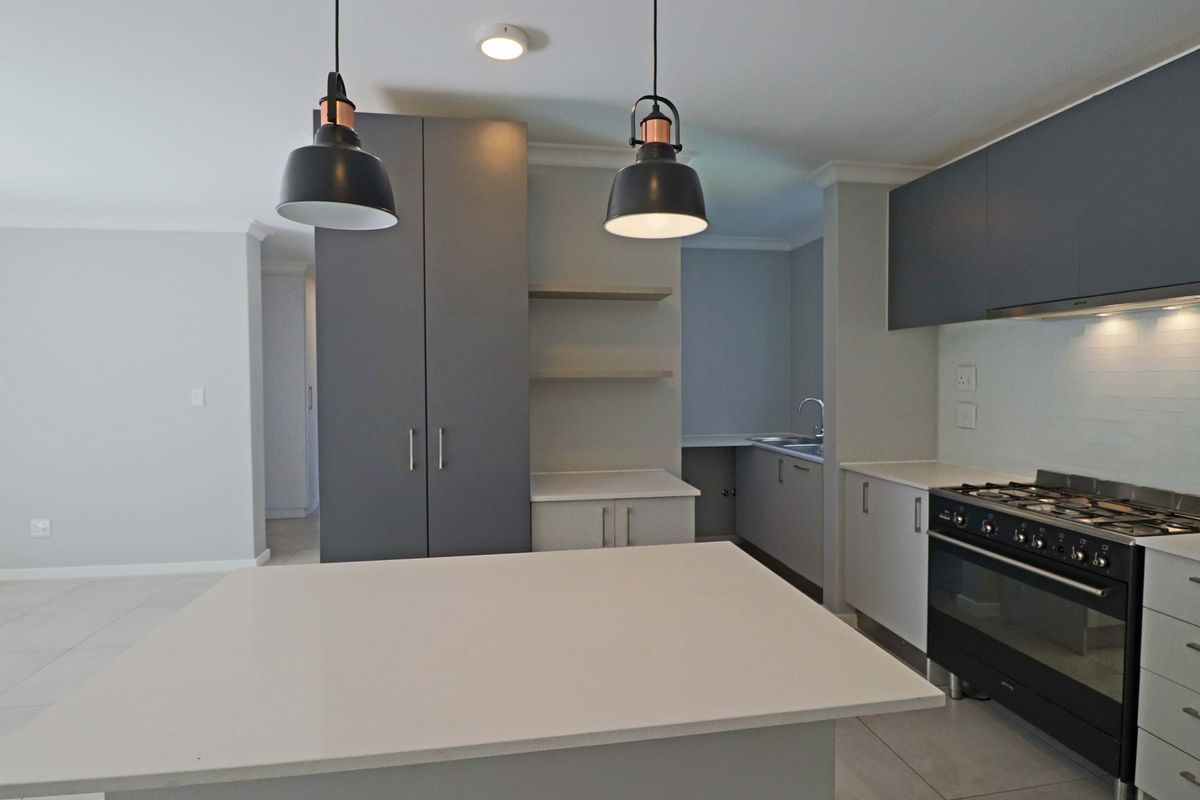Modern kitchen featuring sleek grey cabinetry, stone countertops, a gas stove, and contemporary pendant lighting, offering a clean and functional culinary space.