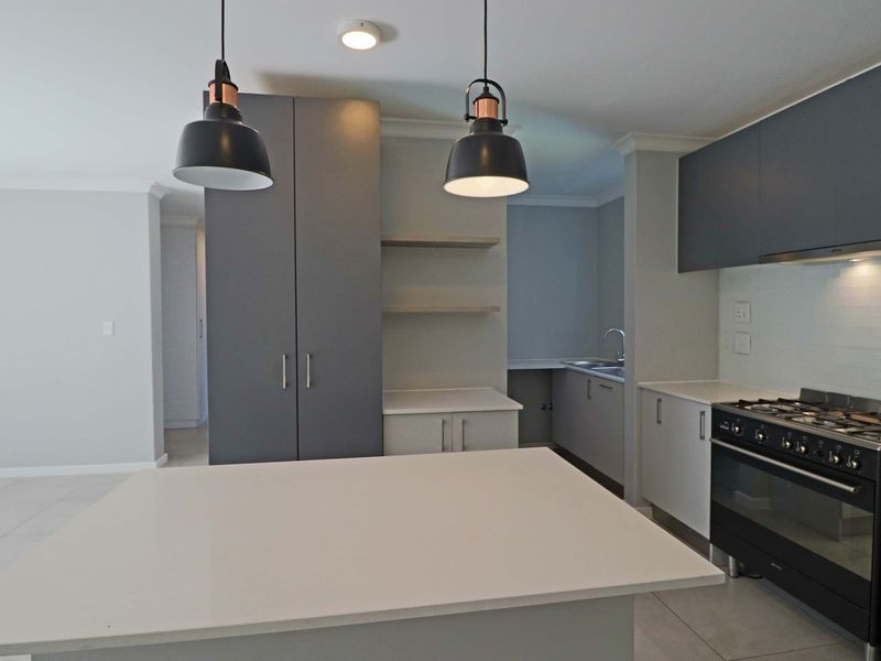 Modern kitchen featuring sleek grey cabinetry, stone countertops, a gas stove, and contemporary pendant lighting, offering a clean and functional culinary space.