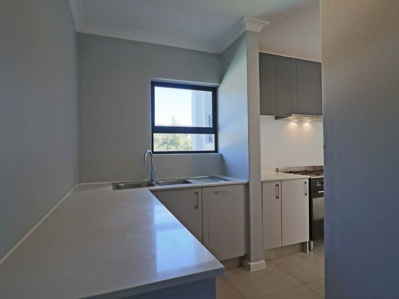A clean, modern kitchen featuring neutral cabinetry, stone countertops, a stainless steel sink, and a built-in gas stove with an extractor fan.