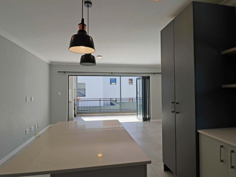 Modern open-plan living area featuring a kitchen island, sleek cabinetry, and large stacking doors leading to a private balcony.