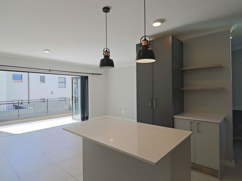 Modern open-plan living area featuring a sleek kitchen island, contemporary cabinetry, tiled floors, and seamless access to a private balcony through folding glass doors.