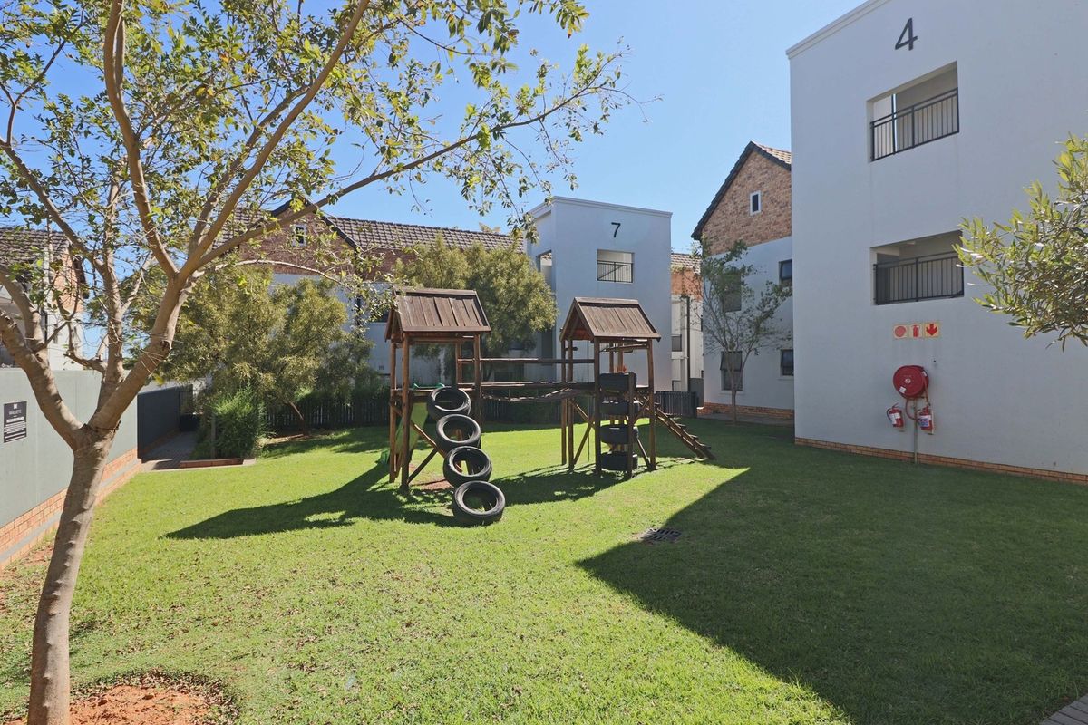 A well-maintained communal garden area between apartment blocks, featuring a children's play structure and essential fire safety equipment mounted on the building exterior.