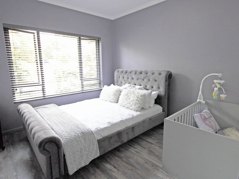 A well-maintained bedroom featuring modern laminate flooring, neutral grey walls, and fitted venetian blinds.