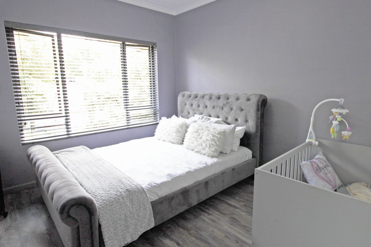 A well-maintained bedroom featuring modern laminate flooring, neutral grey walls, and fitted venetian blinds.