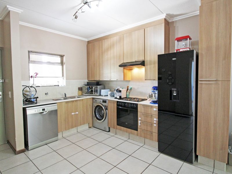 A functional kitchen featuring light wood-finish cabinetry, tiled flooring, a built-in oven with hob, and integrated space for laundry appliances.