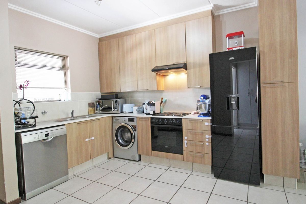 A functional kitchen featuring light wood-finish cabinetry, tiled flooring, a built-in oven with extractor fan, and integrated space for laundry and dishwashing appliances.