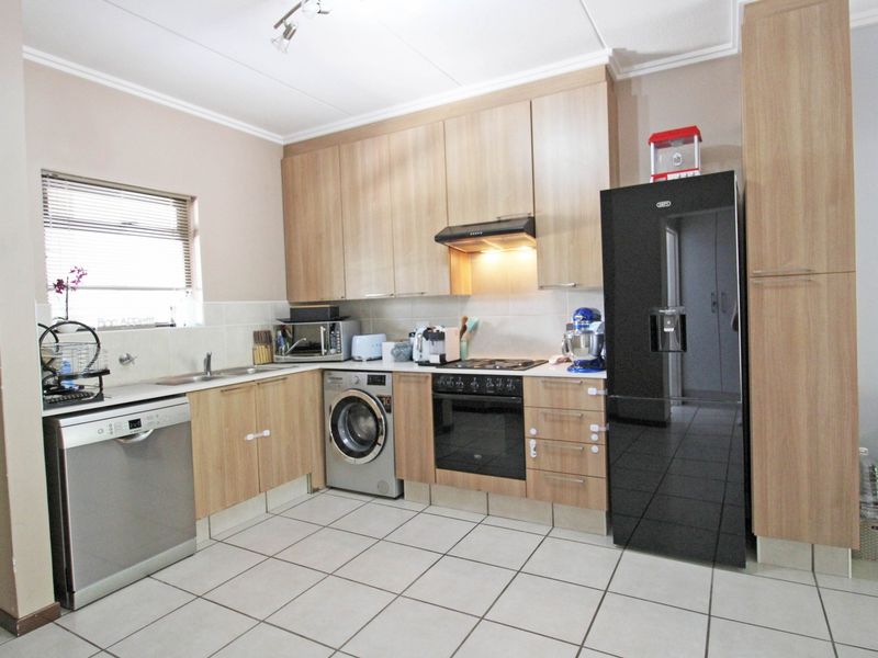 A functional kitchen featuring light wood-finish cabinetry, tiled flooring, a built-in oven with extractor fan, and integrated space for laundry and dishwashing appliances.