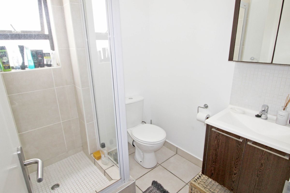 A functional bathroom featuring a shower enclosure, a modern vanity with basin, and neutral floor and wall tiling.