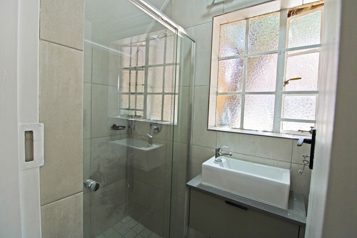 A clean, modern bathroom featuring a glass-enclosed shower, a wall-mounted basin with a vanity cabinet, and tiled walls with a grid-pattern window.