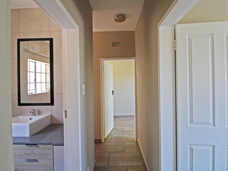 A clean, neutral hallway featuring tiled flooring, providing access to a bathroom with a modern vanity and adjacent rooms.