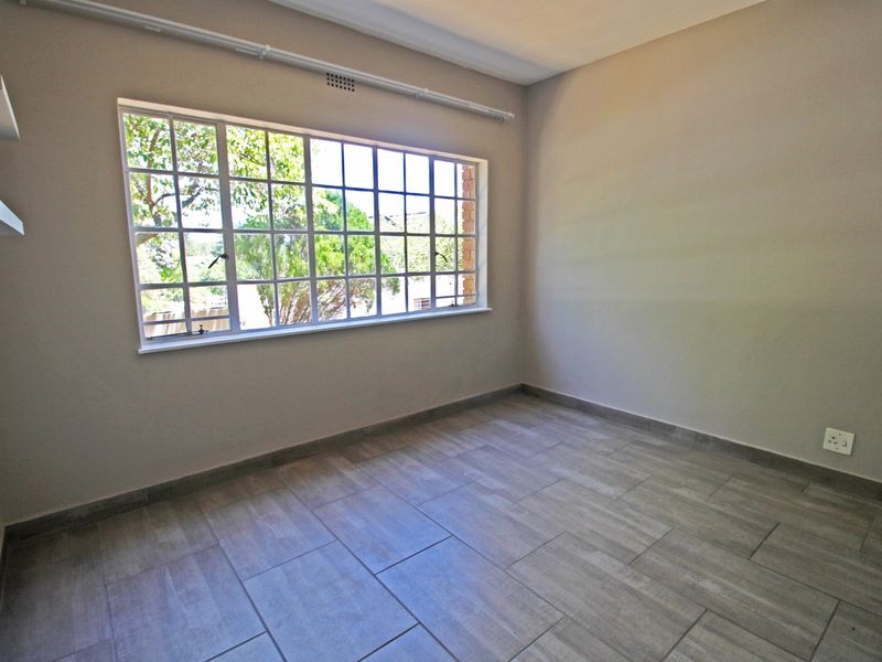 A bright, empty bedroom featuring modern tiled flooring, a large grid-pattern window, and built-in shelving, offering a clean and neutral space.