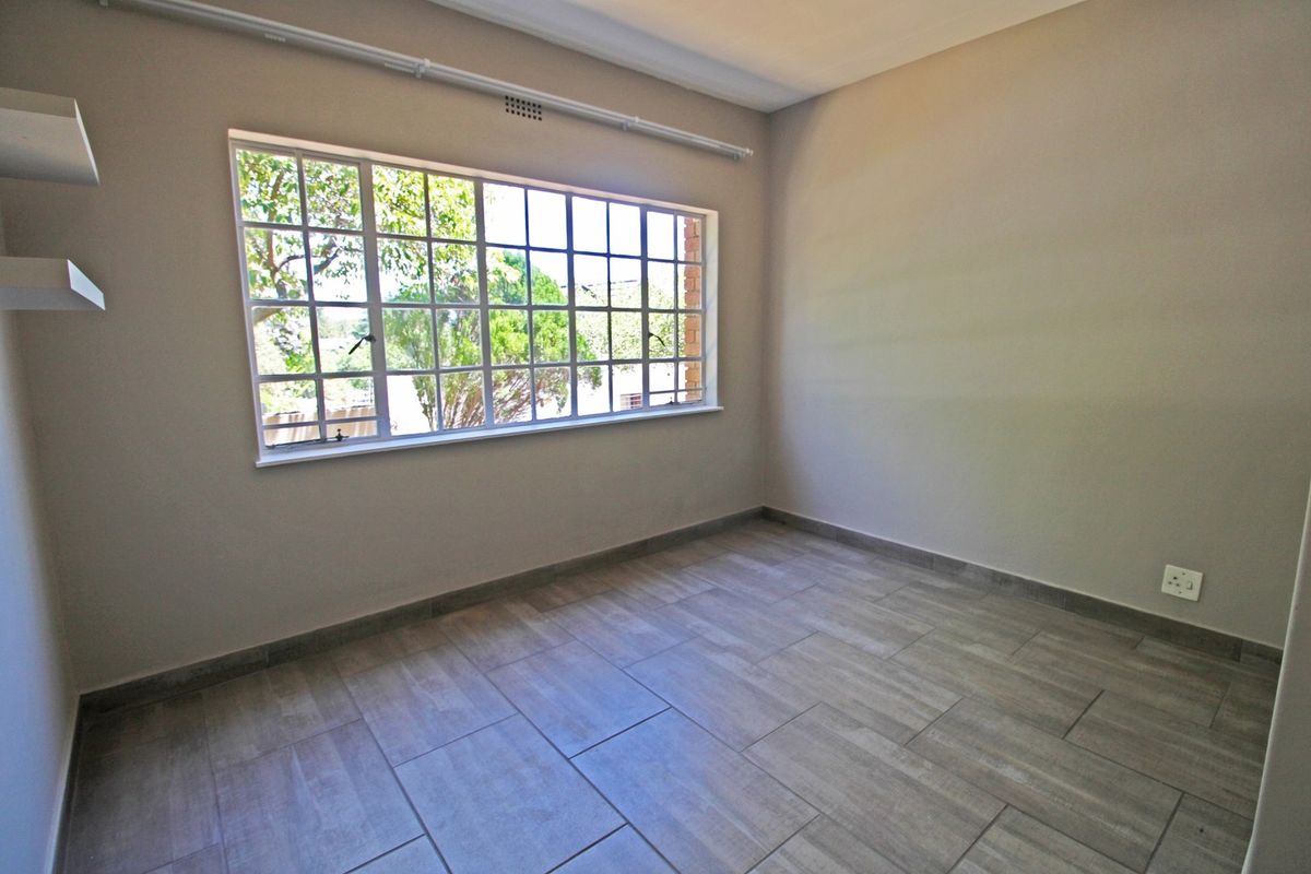 A bright, empty bedroom featuring modern tiled flooring, a large grid-pattern window, and built-in shelving, offering a clean and neutral space.