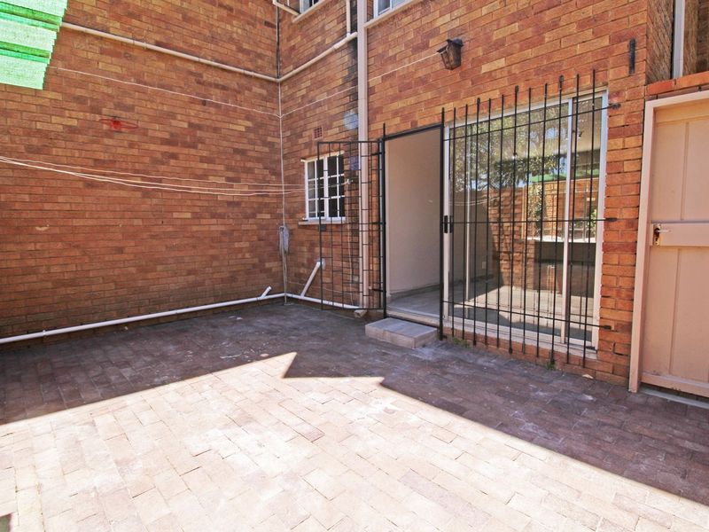 A private paved courtyard area featuring exposed brick walls, secure sliding door access, and external security fixtures, offering a functional outdoor space.