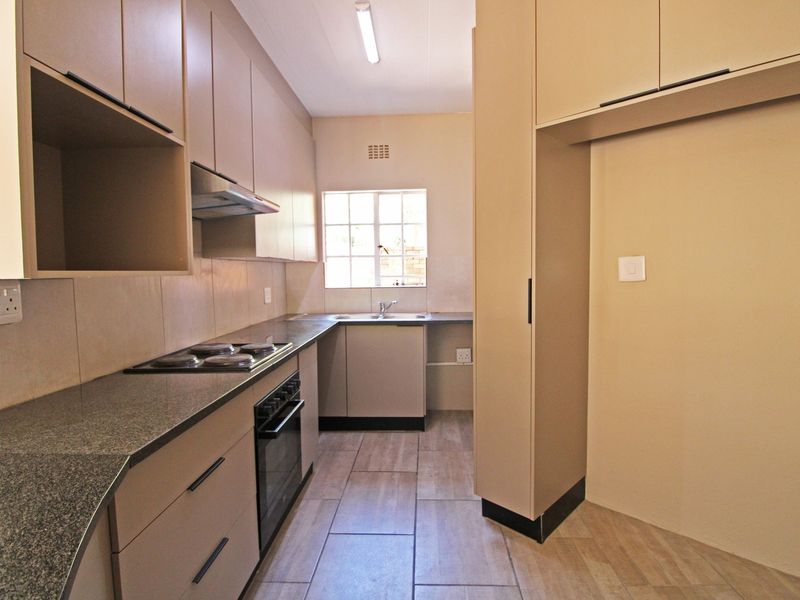 A clean and functional kitchen featuring neutral built-in cabinetry, granite countertops, an integrated oven and hob, and tiled flooring.