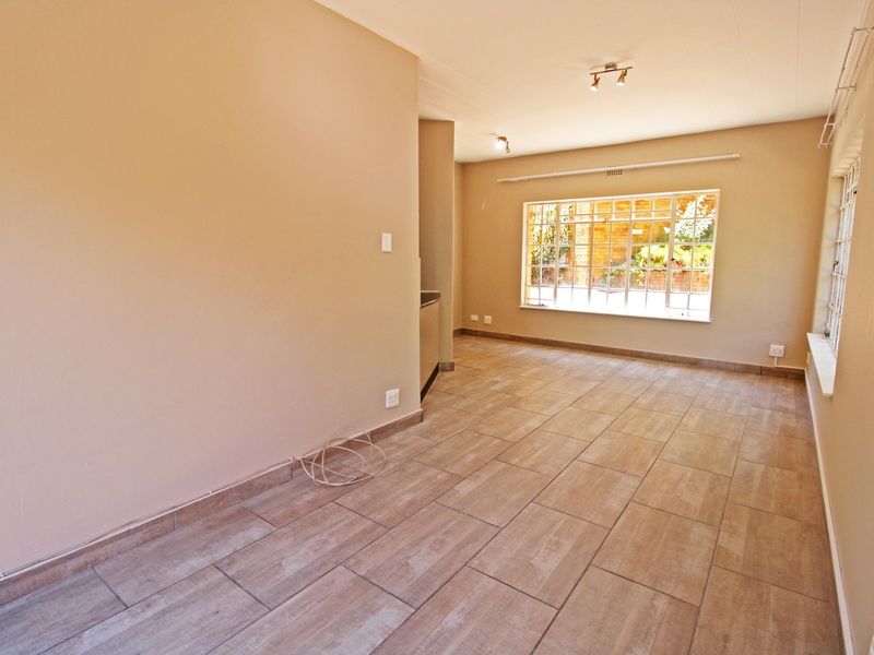 A spacious, empty open-plan living area featuring neutral wall tones, modern wood-look floor tiles, and large windows providing ample natural light.