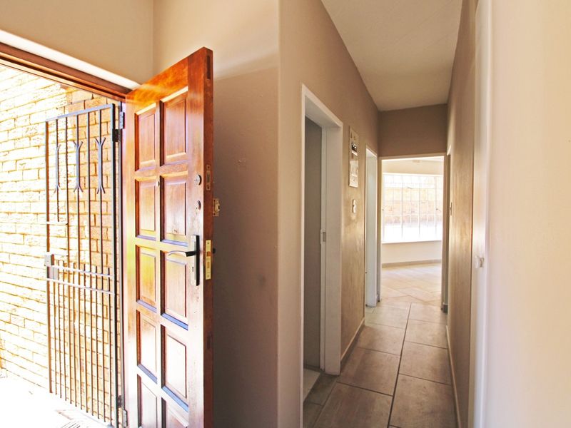 Entrance hallway featuring tiled flooring, a solid timber panelled door, and an integrated security gate, leading into the main living area.