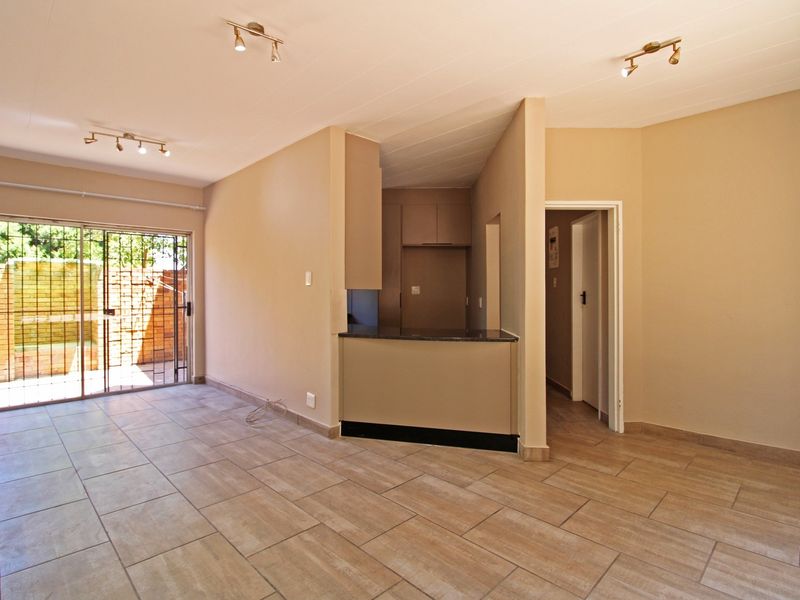 An open-plan living area featuring neutral tiled flooring, a kitchen breakfast bar, and a sliding glass door leading to an outdoor space.