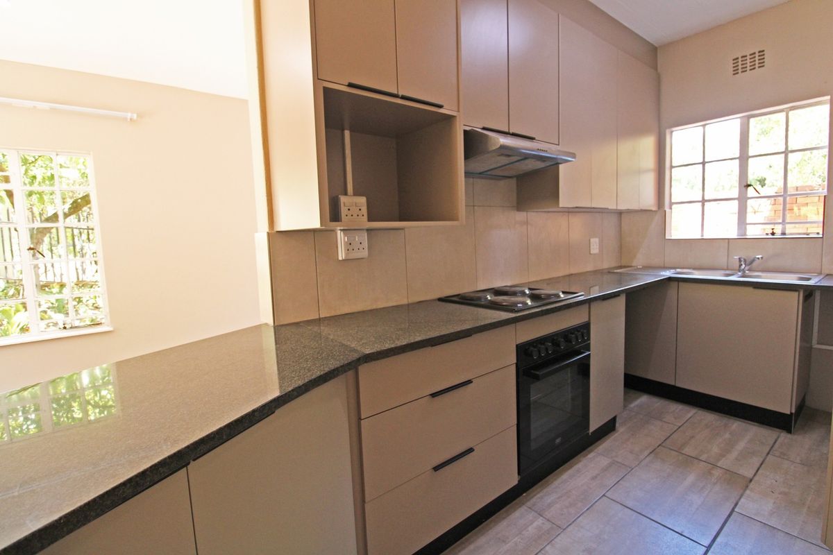 A clean and functional kitchen featuring neutral cabinetry, granite countertops, built-in oven and hob, and tiled flooring with ample natural light.