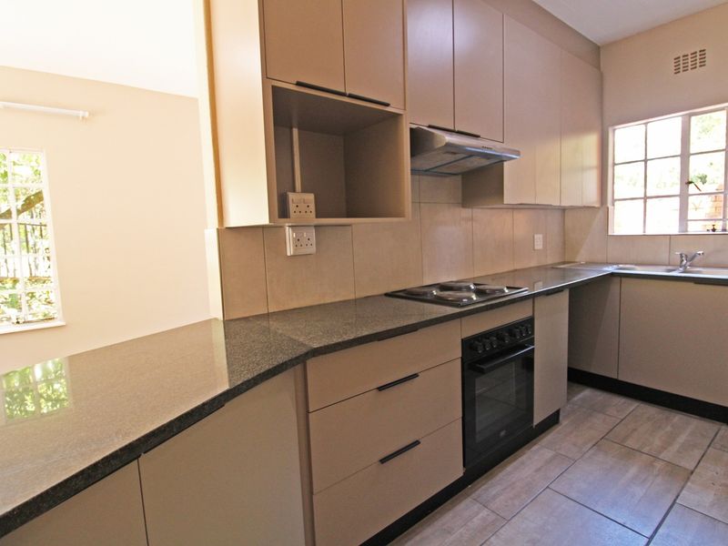 A clean and functional kitchen featuring neutral cabinetry, granite countertops, built-in oven and hob, and tiled flooring with ample natural light.