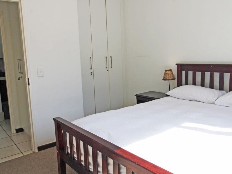 A functional bedroom featuring built-in cupboards and neutral finishes, with an adjacent tiled area visible through the doorway.
