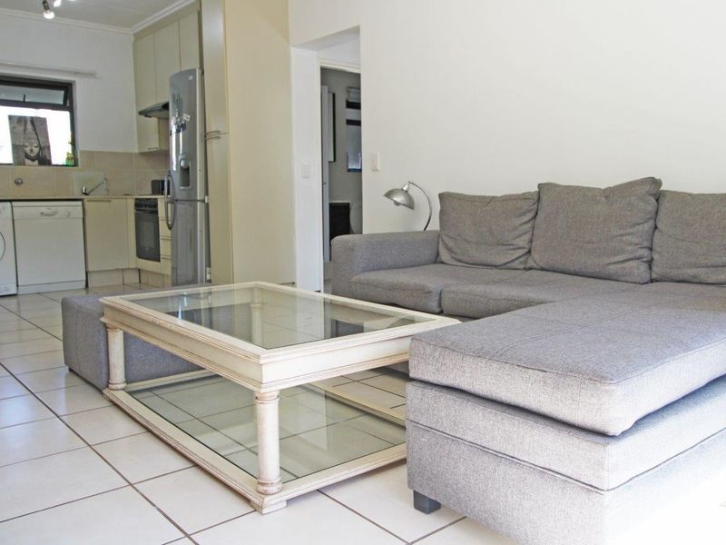An open-plan living area featuring tiled floors and a functional kitchen with built-in cabinetry, oven, and hob, seamlessly connected to the lounge space.