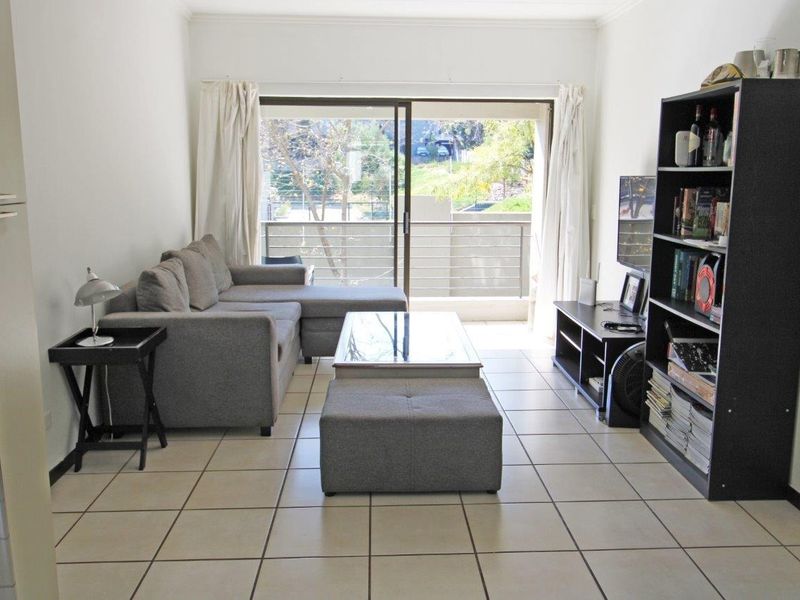 A bright living room featuring tiled flooring and a large sliding glass door that provides direct access to an outdoor balcony area.