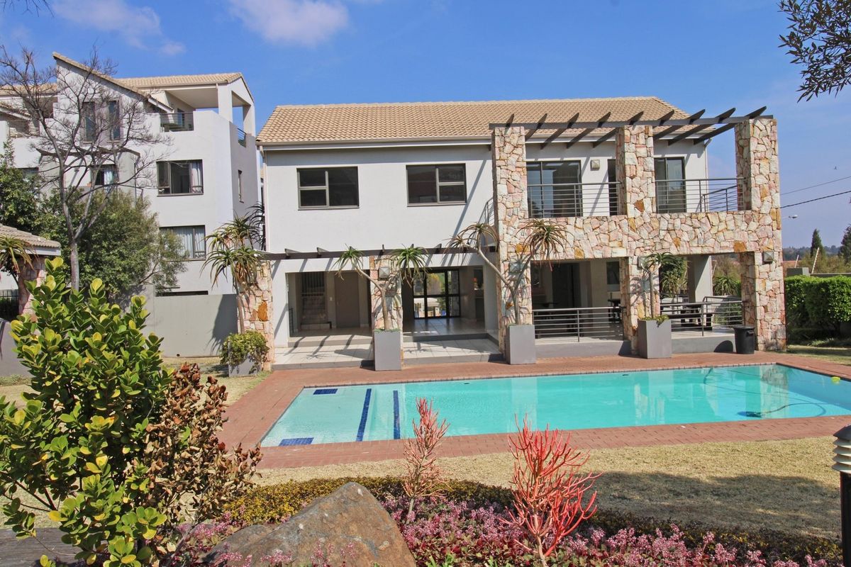 Rear view of the apartment building featuring a swimming pool, stone-clad facade, and a covered patio with an upper-level balcony.
