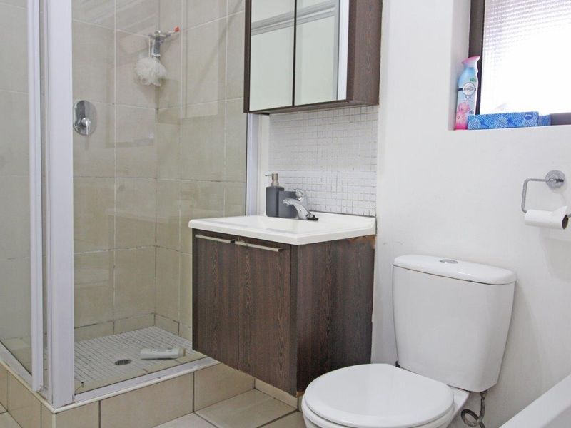 A functional bathroom featuring a shower enclosure, vanity cabinet with basin, wall-mounted storage, and a standard toilet with tiled finishes.