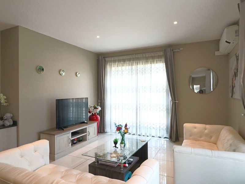 A well-maintained living room featuring tiled flooring, recessed downlighting, and a split-system air conditioner, with direct access to an outdoor area via sliding doors.