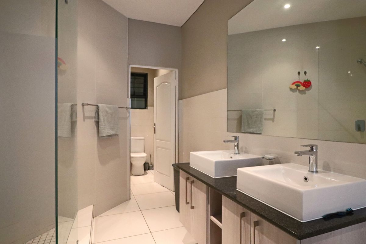Modern bathroom featuring a double vanity with vessel sinks, granite countertops, a large wall mirror, and a separate glass-enclosed shower area.
