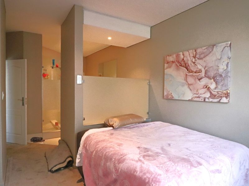 A bedroom featuring a partition wall separating the sleeping area from an en-suite bathroom, with neutral wall tones and recessed ceiling lighting.