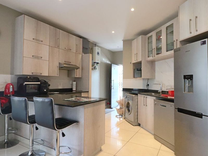 Modern kitchen featuring light wood-finish cabinetry, granite countertops, tiled flooring, and integrated space for appliances, offering a functional and contemporary cooking area.