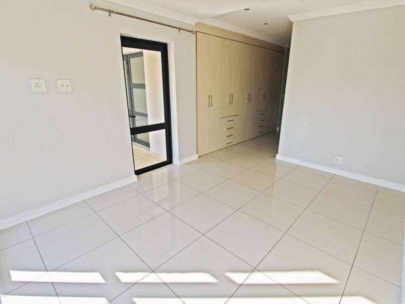 A bright, empty bedroom featuring modern tiled flooring, extensive built-in cupboards, and clean neutral finishes, ready for personalization.