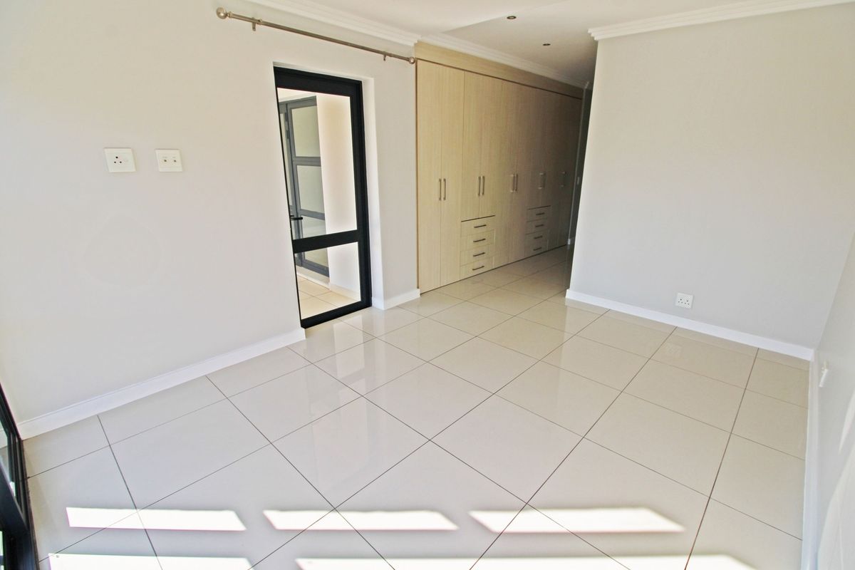 A bright, empty bedroom featuring modern tiled flooring, extensive built-in cupboards, and clean neutral finishes, ready for personalization.