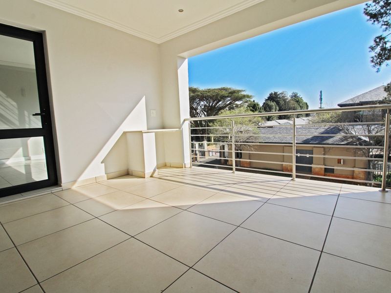A spacious, covered balcony featuring neutral floor tiles, a modern stainless steel balustrade, and a built-in counter, offering a clean and well-maintained outdoor space.