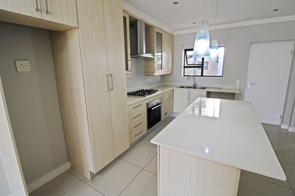 Modern kitchen featuring light wood cabinetry, stone countertops, a central island, and integrated appliances including a gas hob and oven.